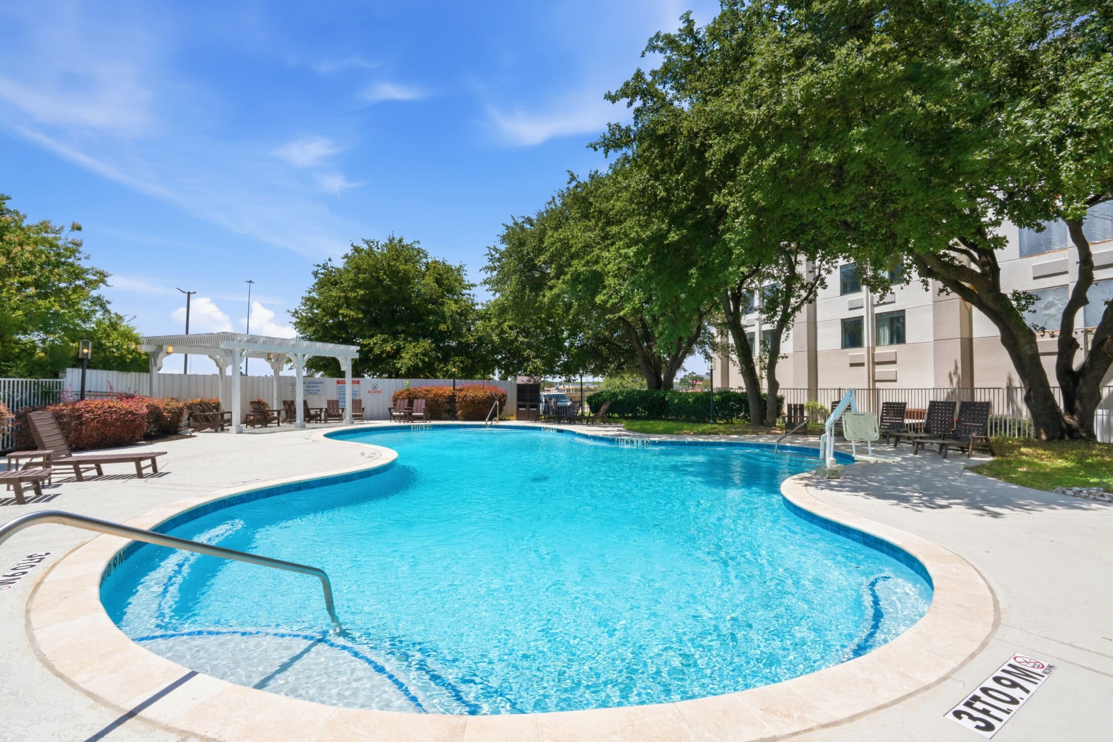 A curved outdoor pool with lounge chairs and trees in the background.